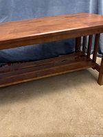 Front angle view of a medium brown wooden mission style coffee table with slatted sides and lower shelf.