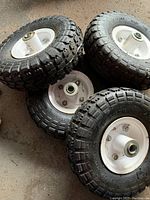 Four new utility tires on rims, showing tread and white metal rims with central hub bearings.