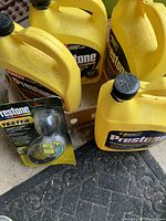 Four yellow Prestone Antifreeze gallon jugs, three full and one partially full, arranged upright with black caps, next to a Prestone Antifreeze Tester in its original plastic and cardboard packaging.