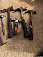 Front view of six hammers laid out on carpet showing different sizes and handle materials, some with paint chips and rusted heads.