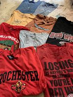Overview of the 10 men's XL T-shirts laid out showing different colors and designs including sports team, cycling, and graphic prints.