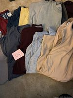 Photo of 15 men's long sleeve heavy t-shirts and tops in XL size, showing variety of colors like gray, maroon, beige, yellow, navy blue. Piled on carpeted floor.
