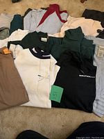 Photo showing a variety of men's XL long sleeve shirts in multiple colors and styles laid out on carpet, including a used and new shirt mix.