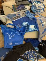 Overview of lots visually showing Detroit Lions themed shirts, sweatshirts, tote bags, serving tray, ceramic mug, and promotional materials.