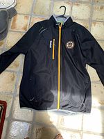 Front view of black Boston Bruins lightweight jacket with yellow zipper, Reebok chest pocket, and team logo on left chest.