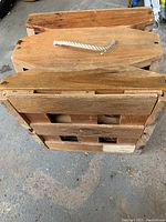 Top and side view of closed wooden case with rope handle.