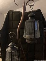 Photo showing two of the hanging metal lanterns with glass panes and a section of the curved decorative metal pole