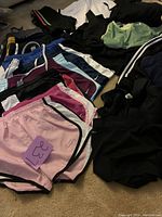 Overview of workout shorts in various colors laid out on floor showing multiple pairs including pink, burgundy, blue, black, white with Nike logos and trim