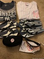 Photo showing two women's small Yankees T-shirts, two pairs of flip-flops with Yankees logos, sunglasses case, and sunglasses with pouch.