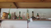 Shelf displaying seven assorted vintage or decorative liquor bottles and barware.