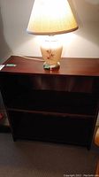 Photo of wooden bookcase with a dark finish and two shelves with lamp on top
