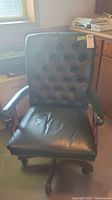 Front view of black leather office chair showing padded seat, tufted back, and armrests.
