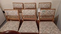 Front view of all six wooden dining chairs with floral upholstery on seats and backs.