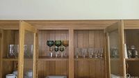 A collection of crystal and colored stemware glasses arranged on wooden shelves inside a cabinet.