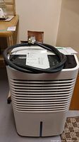 Front angled view of white Whirlpool Gold dehumidifier with black control panel and attached black hose coiled on top.