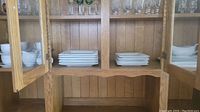 Wooden cabinet with shelves containing stacks of white plates and bowls.