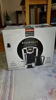 Front view of original box packaging showing the Keurig 2.0 coffee maker, carafe, and K-Cups.