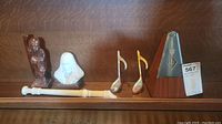 Full view of metronome, recorder, brass musical notes, and two figurines all displayed on wooden shelf