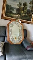 Mirror resting on a chair, showing its overall shape and wooden frame with decorative etched patterns.