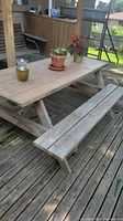 Full view of the wooden picnic table with plants on top, positioned on a wooden deck outdoors.