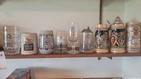 Shelf with 8 assorted beer steins and glasses with different brands and styles visible
