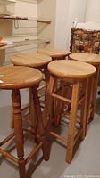 Five wooden bar stools grouped together. Two different leg styles visible, natural wood finish.