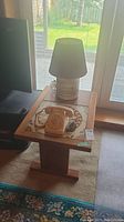 Wood table with decorative tile, vintage lamp on top, beige rotary phone beside the lamp, room setting