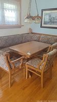 Photo showing corner-style upholstered bench seating around rectangular wooden dining table with two visible chairs.