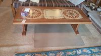 Front angle view of vintage wooden coffee table with two circular floral patterned tile insets and one central decorative tile inset on top, placed on light carpeted floor with patterned rug nearby.