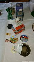 Overview photo showing assortment of tins, figurines, plates, and model car on display surface.