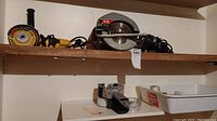 Two shelves showing Dewalt angle grinder, Skil circular saw, tape bin, and tape tools on the lower shelf. Black & Decker drill is mostly visible.