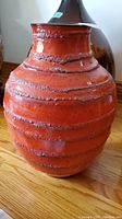 Side view of ceramic vase showing textured horizontal bands and orange color