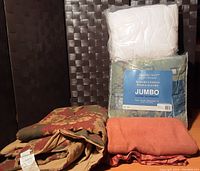 Photo of folded bedding including packaged Mainstays reversible comforter, floral patterned blanket, burnt orange blanket, and white pillow