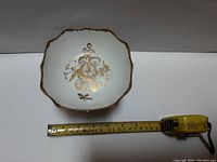 Top view of Birks pedestal dish showing scalloped edges and gold floral motif with measuring tape indicating size.