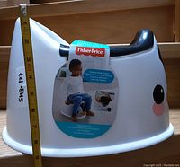 Side view showing the height measurement with a tape measure against the potty. Sticker on the side with brand and usage info.