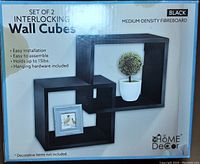 Box labeling showing set of 2 black interlocking wall cubes made from medium density fibreboard with easy installation and up to 15 lbs weight capacity.