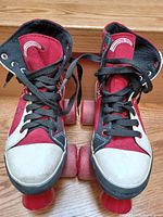 Front view of the roller skates showing red, black and white canvas boots, black laces, white toe caps, and red wheels. Some scuffing visible on the toe area.