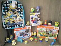 Photo of all items including Minions backpack, three boxed Mega Construx sets and multiple Minions figurines arranged on a flat surface against a wall.