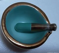 Top-down view of small turquoise ceramic mortar with metallic gold rim and matching pestle with metallic handle and turquoise grinding tip.