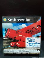 Front face of unopened puzzle box featuring bright red Lockheed Model 5B Vega airplane image and 500 piece count.