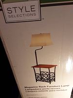 Box showing Style Selections logo and product image of the magazine rack furniture lamp with fabric shade and bronze/dark oak finish.