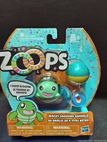 Front view of the Zoops turtle toy in original packaging showing the toy and colorful background with product branding and warnings.