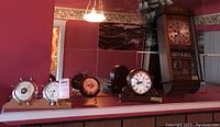 Photo showing the collection of barometers and clocks on a shelf, including the Esgrad wooden wall clock, Bulova quartz mantle clock, Barigo barometer, and Airguide barometer.