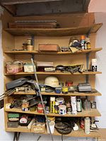 Wide view of wooden shelves holding numerous cans, boxes, small tools, and supplies including a white hard hat and spray cans.