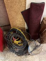 Photo showing extension cords coiled on the floor along with a rolled rubber-backed mat and empty metal Freon tank.