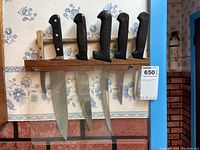 Six knives displayed in a wooden wall-mounted holder with blades hanging down.