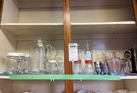 Shelf view showing multiple glassware items including drinkware mugs, cruets, salt and pepper shakers, and measuring cups.