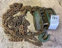 Green metal chain hoist with rusted chains and large hook on floor, labeled 1 Ton Hoist