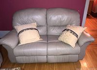 Front view of beige leather reclining loveseat with two beige cushions against red wall, hardwood floor.