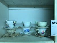 Photo of 6 vintage porcelain teacups with matching saucers arranged in two rows. Each cup has floral designs and gold trim. Brands include Grafton Grasmere, Colclough, Regina, and Queen Anne.